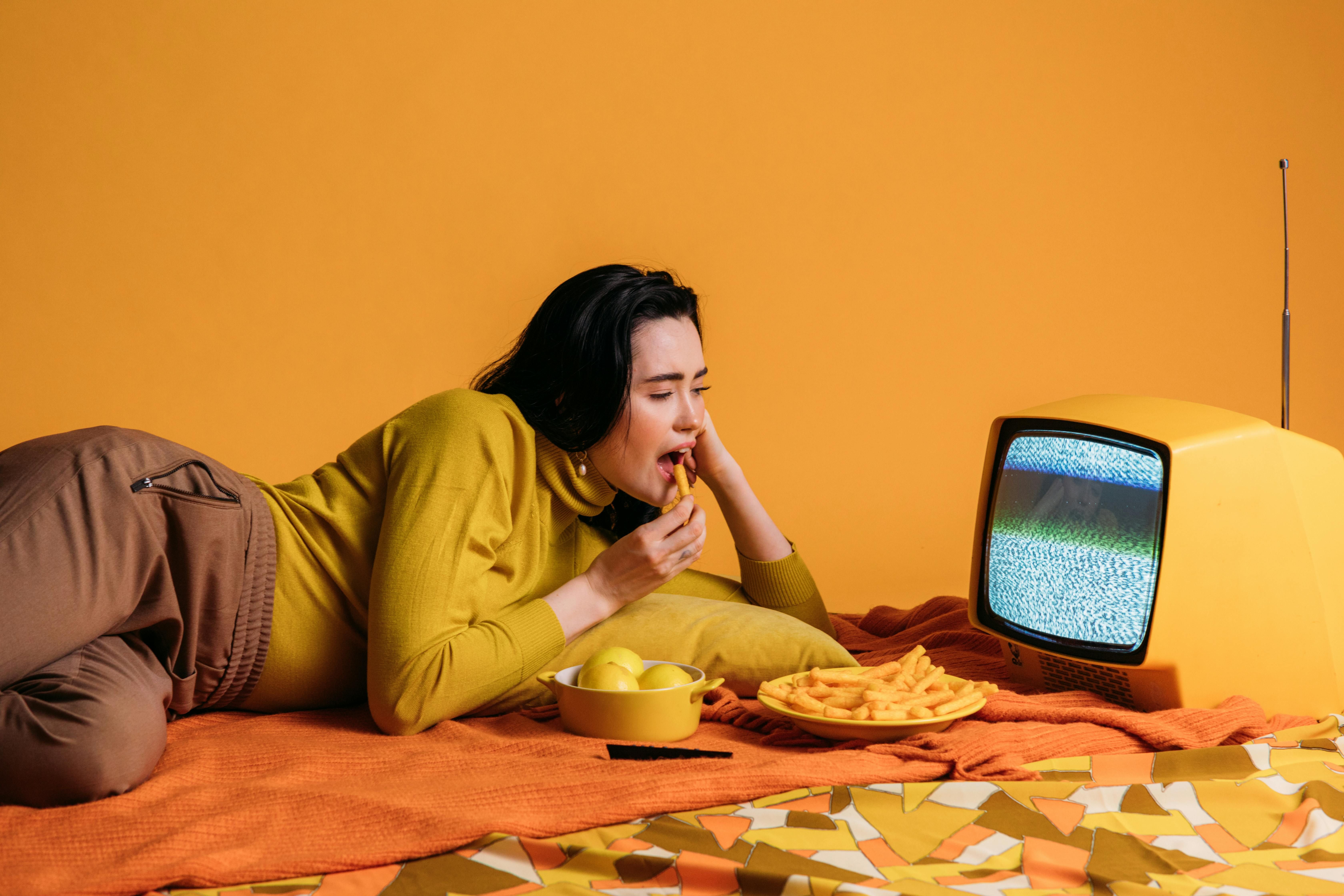 Managing Emotional Eating: Overcoming TV-Induced Food Cravings for Healthier Habits A woman emotionally eating in front of the TV, highlighting the challenges of managing food cravings while watching television.