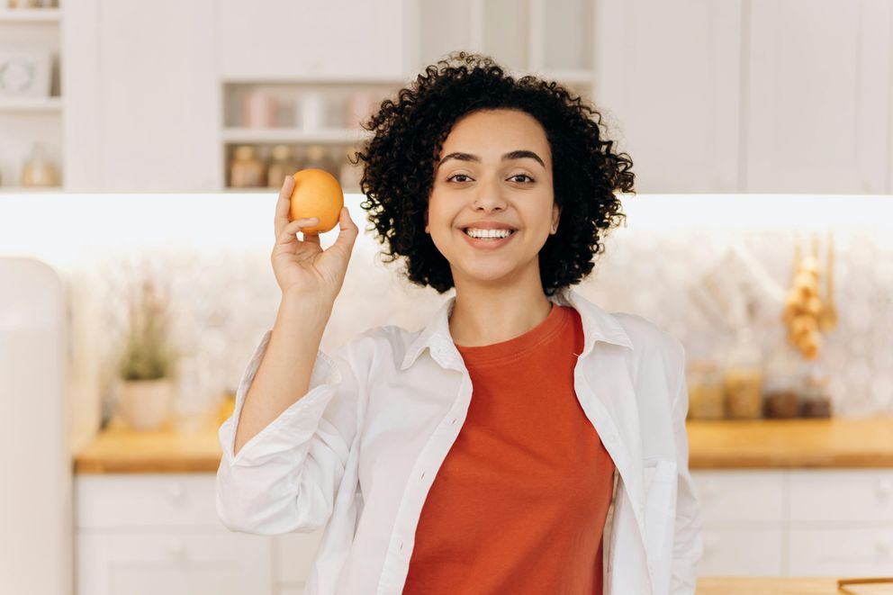Starting Keto and IF with a Smile: Woman's Healthy Choice Joyful woman embarking on keto and intermittent fasting journey with an orange in hand