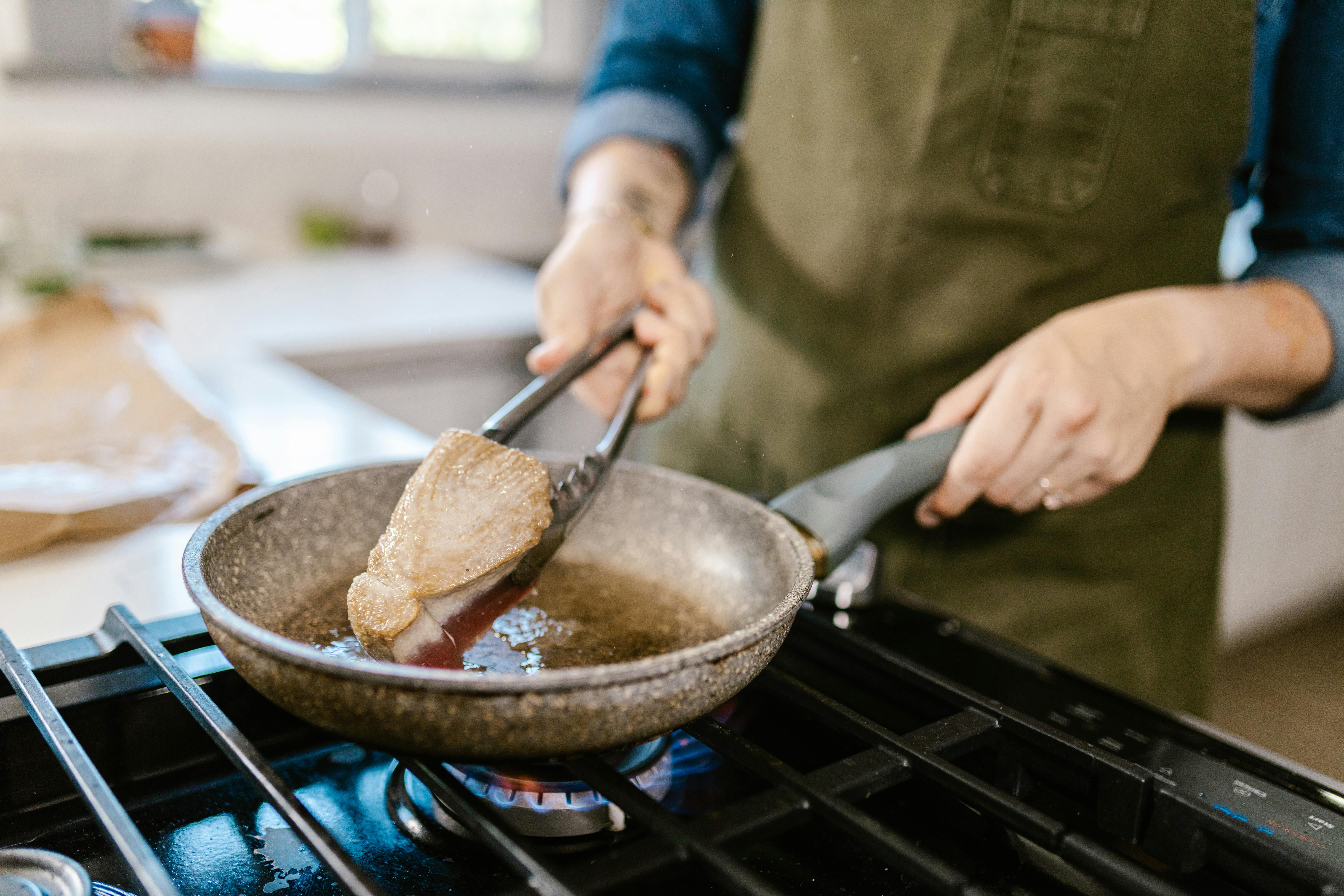 Woman Frying Meat for the Carnivore Diet A woman frying meat in a pan on the stove.